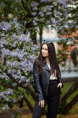 Gülen ve gülümseyen güzel, mutlu, uzun saçlı model kız yaz leylak bahçesinde kameraya poz veren çiçekler. Saç konseptiyle oynamak.
