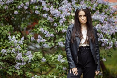 Gülen ve gülümseyen güzel, mutlu, uzun saçlı model kız yaz leylak bahçesinde kameraya poz veren çiçekler. Saç konseptiyle oynamak.