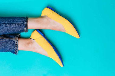 Güzel kadın bacakları şık sarı ayakkabılar giyer, topuksuz. Açık sarı yaz sandaletleri mavi arka planda.