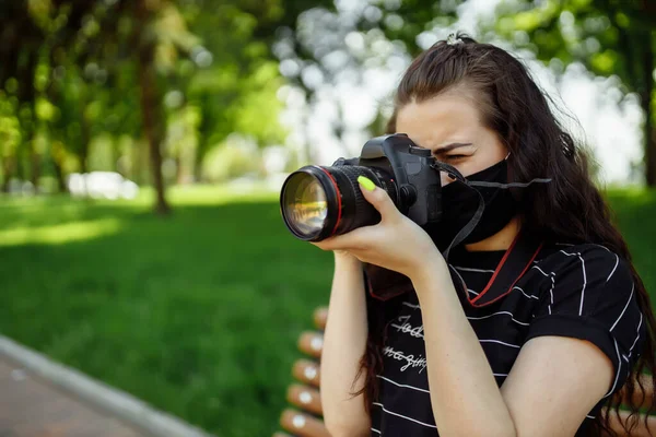 Beautiful girl with a camera wears a medical mask and takes pictures in the park. Coronavirus 2019 nCoV pneumonia outbreak — Stock Photo, Image