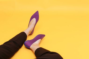 Güzel kadın bacakları şık mor düz ayakkabılar giyer. Sarı arka planda mor sandaletler.
