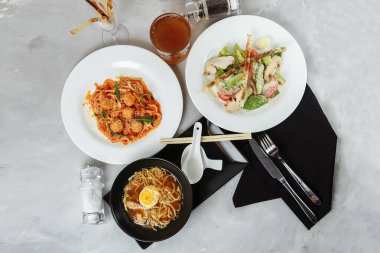 Lokantada bir masada üç çeşit menü. Tavuk ve yumurtalı ramen, taze sezar salatası ve makarna..
