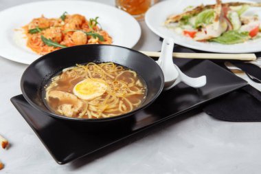 Lokantada bir masada üç çeşit menü. Tavuk ve yumurtalı ramen, taze sezar salatası ve makarna..