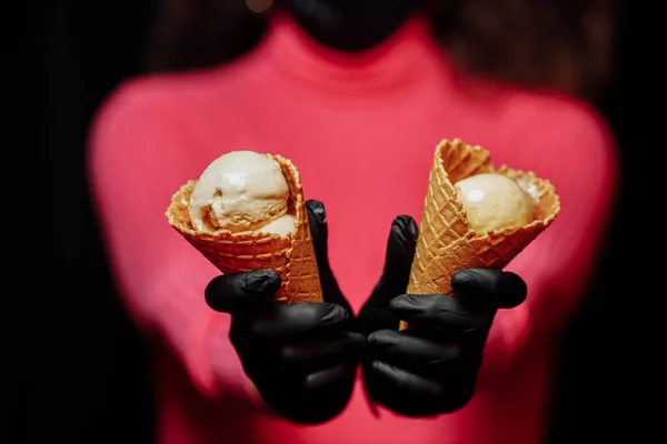 Siyah koruyucu eldivenli eller dondurmalı waffle külahını tutuyor. Koronovirüse karşı koruma. Karantina sırasında dondurma satma kavramı. Dondurma ellerinde koruyucu siyah eldivenlerle.
