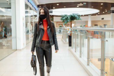 Siyah maskeli bir kız alışveriş merkezi boyunca yürüyor. Koronavirüs salgını. Koruyucu maskeli bir kız alışveriş merkezinde alışveriş yapıyor.