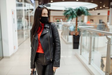 Siyah maskeli bir kız alışveriş merkezi boyunca yürüyor. Koronavirüs salgını. Koruyucu maskeli bir kız alışveriş merkezinde alışveriş yapıyor.
