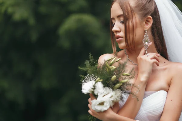 Pengantin wanita cantik dengan gaun pengantin megah berpose di antara tanaman hijau di jalan. Konsep pengantin untuk gaun iklan — Stok Foto