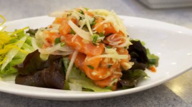 Hareket tarafından ahşap masa üzerinde beyaz tabak salata sebze ile taze çiğ taze somon.