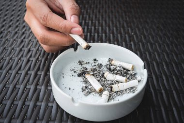Bir kül tablası masada sigara koyarak el.