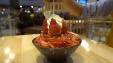 Bingsu, kesilmiş buz ile biraz süt krem krem peynir ve taze çilek ile tepesinde. Kadın el yoğunlaştırılmış süt yığını. Ağır çekim 120p