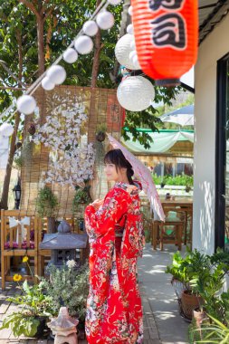 Kız, Japonya 'nın ulusal elbisesi olan geleneksel kırmızı bir kimono giyiyor ve bir şemsiye tutuyor.