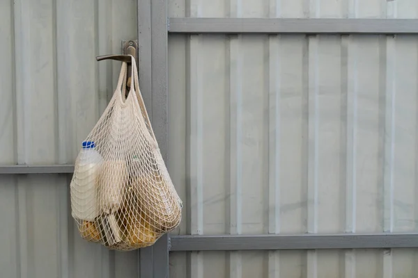 Food delivery. A cotton mesh bag for products with cereals, vegetable oil and milk hangs on a fence. Zero waste, no plastic purchases. Sustainable lifestyle concept. Recycling