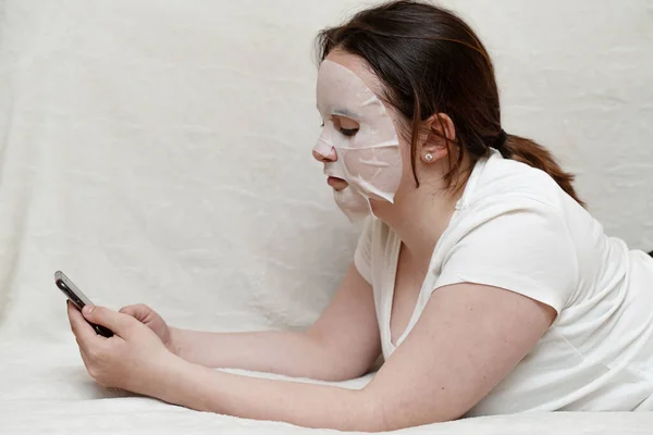 Uma Jovem Mulher Uma Máscara Tecido Cosmético Está Sofá Uma — Fotografia de Stock