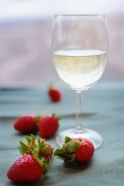 Glass of white wine with strawberries on the background of the window