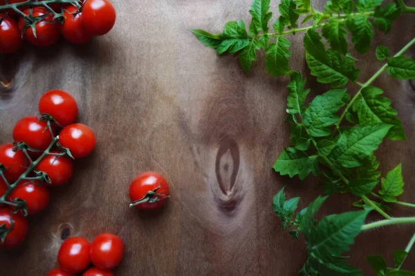 Fresh cherry tomatoes with leaves spread out on a dark wooden background