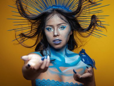 İlham perisi vücut resmi yapıyor sarı fotoğraf stüdyosu arka planında ve farklı ışıklarla oynuyor ve poz veriyor.