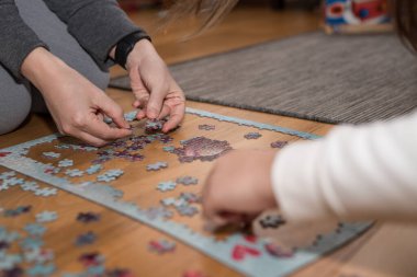 Anne ve kızı, Cornavirus covid-19 yüzünden evin zemininde bir yapbozla oynuyorlar.