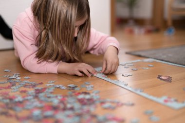 Pembe kazaklı sarışın kız, Coronavirus covid-19 'un nezaretinde yerde yapbozla oynuyor.