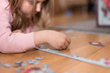 Pembe kazaklı sarışın kız, Coronavirus covid-19 'un nezaretinde yerde yapbozla oynuyor.