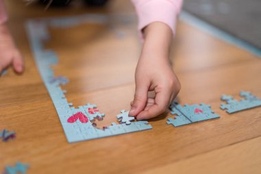 Pembe kazaklı sarışın kız, Coronavirus covid-19 'un nezaretinde yerde yapbozla oynuyor.