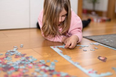 Pembe kazaklı sarışın kız, Coronavirus covid-19 'un nezaretinde yerde yapbozla oynuyor.