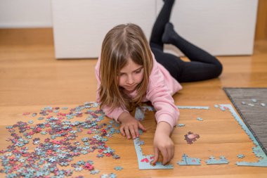 Pembe kazaklı sarışın kız, Coronavirus covid-19 'un nezaretinde yerde yapbozla oynuyor.