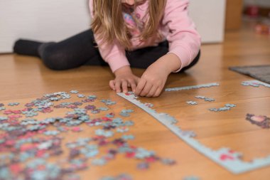 Pembe kazaklı sarışın kız, Coronavirus covid-19 'un nezaretinde yerde yapbozla oynuyor.