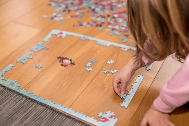 Pembe kazaklı sarışın kız, Coronavirus covid-19 'un nezaretinde yerde yapbozla oynuyor.