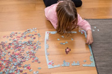 Pembe kazaklı sarışın kız, Coronavirus covid-19 'un nezaretinde yerde yapbozla oynuyor.