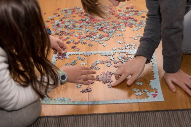 Anne ve kızı, Cornavirus covid-19 yüzünden evin zemininde bir yapbozla oynuyorlar.