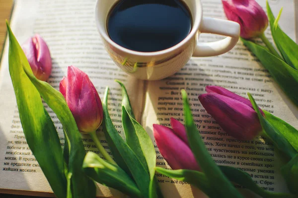 Pencerede koyu, lezzetli, aromatik bir kahve, ilginç bir kitap ve pembe laleler var. Sabah güneşi bir kitabın ve aromatik kahvenin üzerinde parlıyor ve yakınlarda güzel pembe laleler uzanıyor.