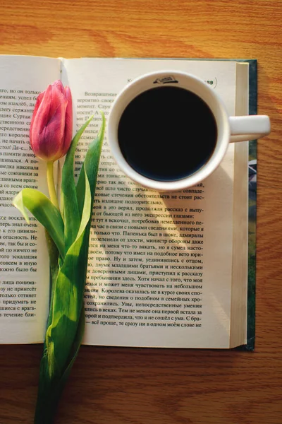 Pencerede koyu, lezzetli, aromatik bir kahve, ilginç bir kitap ve pembe laleler var. Sabah güneşi bir kitabın ve aromatik kahvenin üzerinde parlıyor ve yakınlarda güzel pembe laleler uzanıyor.