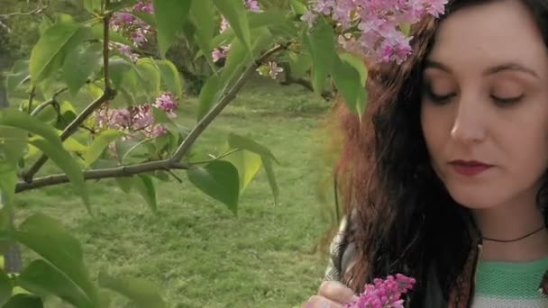 Две девушки нюхают сиреневые цветы в зеленом парке — стоковое видео