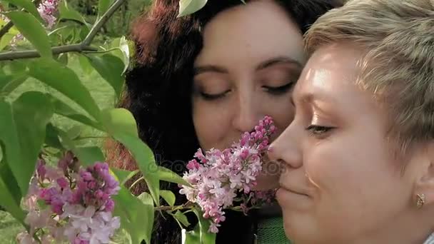 Δύο κορίτσια sniffing ιώδη λουλούδια στο καταπράσινο πάρκο — Αρχείο Βίντεο