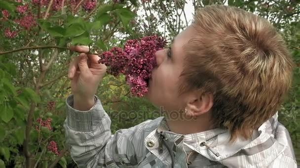 Mooi blond meisje snuiven lila bloemen in park — Stockvideo