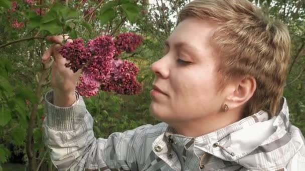 Linda chica rubia oliendo flores de lila en el parque — Vídeos de Stock