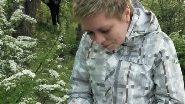 Pretty blond girl looks at flowers in a green park — Stock Video