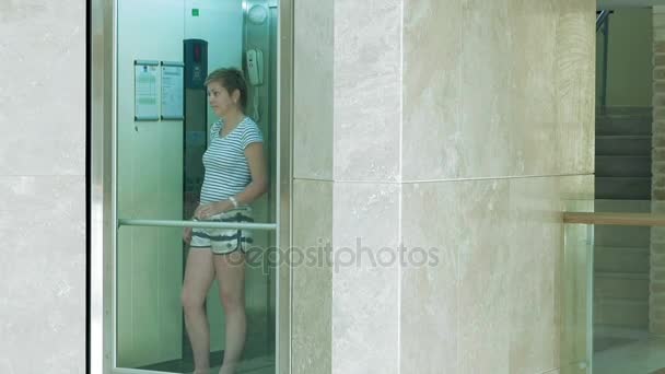 Женщина стоит в стеклянном подъёмнике — стоковое видео