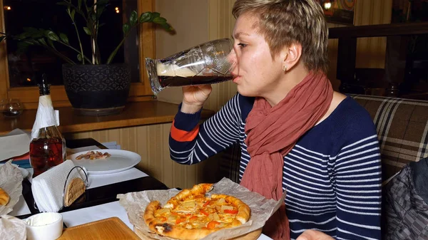 Pretty blond woman eats pizza and drinks beer — Stock Photo, Image