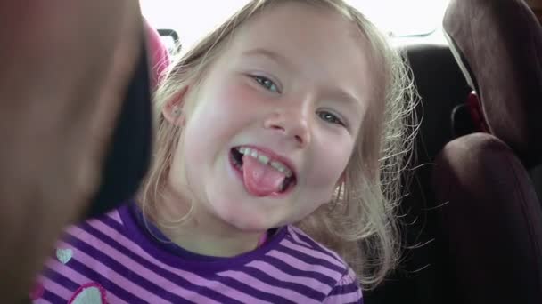 Liten flicka i en bilbarnstol för barn ler och skrattar — Stockvideo