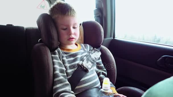 Rapaz bonito em um assento de carro de criança brinca com um brinquedo — Vídeo de Stock
