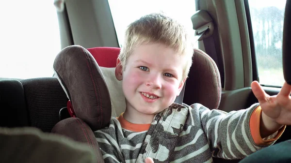 Garoto bonito em um assento de carro de criança sorri e ri — Fotografia de Stock