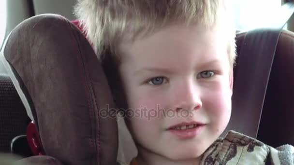 Garoto bonito em um assento de carro de criança sorri e ri — Vídeo de Stock