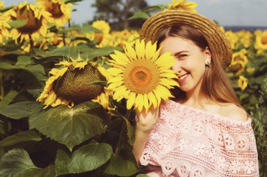 Beyaz gömlekli güzel, gülümseyen genç bir kadın tarlada ayçiçeklerinin arasında duruyor..