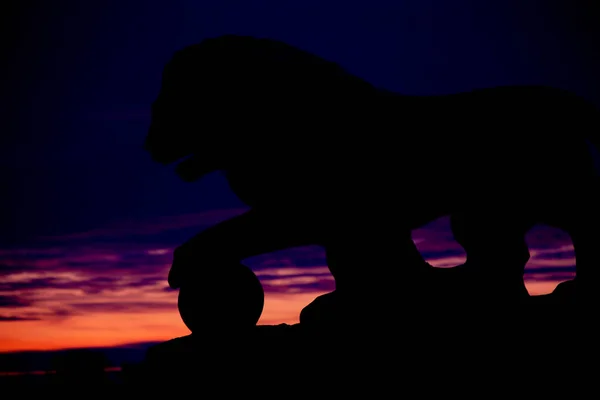 Statue of a lion at sunset on a very dark background. Creative background for your website, business card, poster with space for an inscription or logo