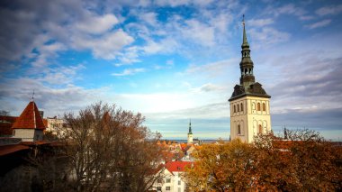 Tallinn 'in sonbahar panoraması kale duvarından. Kilise kulesi manzarası, sonbahar ağaçları ve kale duvarı. Bulutlu mavi gökyüzü