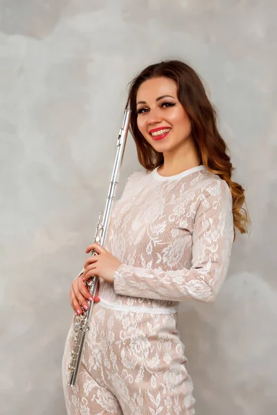Woman with flute. Girl actress in suit with flute on light background. Flute in hand. Concept of musical design. Girl smiles and looks at photocamera