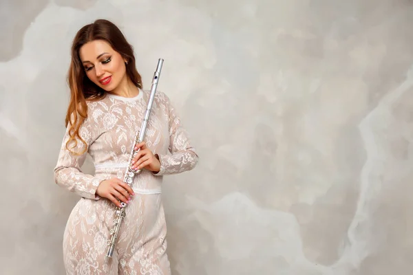 Woman with flute. Girl actress in suit with flute on light background. Flute in hand. Concept of musical design. With place in photo for your lettering or logo