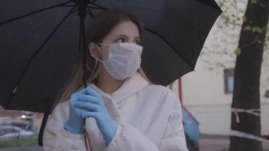 Tıbbi maske takan ve şemsiye altında lastik eldiven takan bir kız. Kötü havada sokakta maske takan bir kadın. Genç bayan Slav 'ın yakın çekimi. Virüs koruması kavramı. Covid-19 salgını