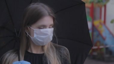 Tıbbi maske takan ve şemsiye altında lastik eldiven takan bir kız. Kötü havada sokakta maske takan bir kadın. Genç bayan Slav 'ın yakın çekimi. Virüs koruması kavramı. Covid-19 salgını